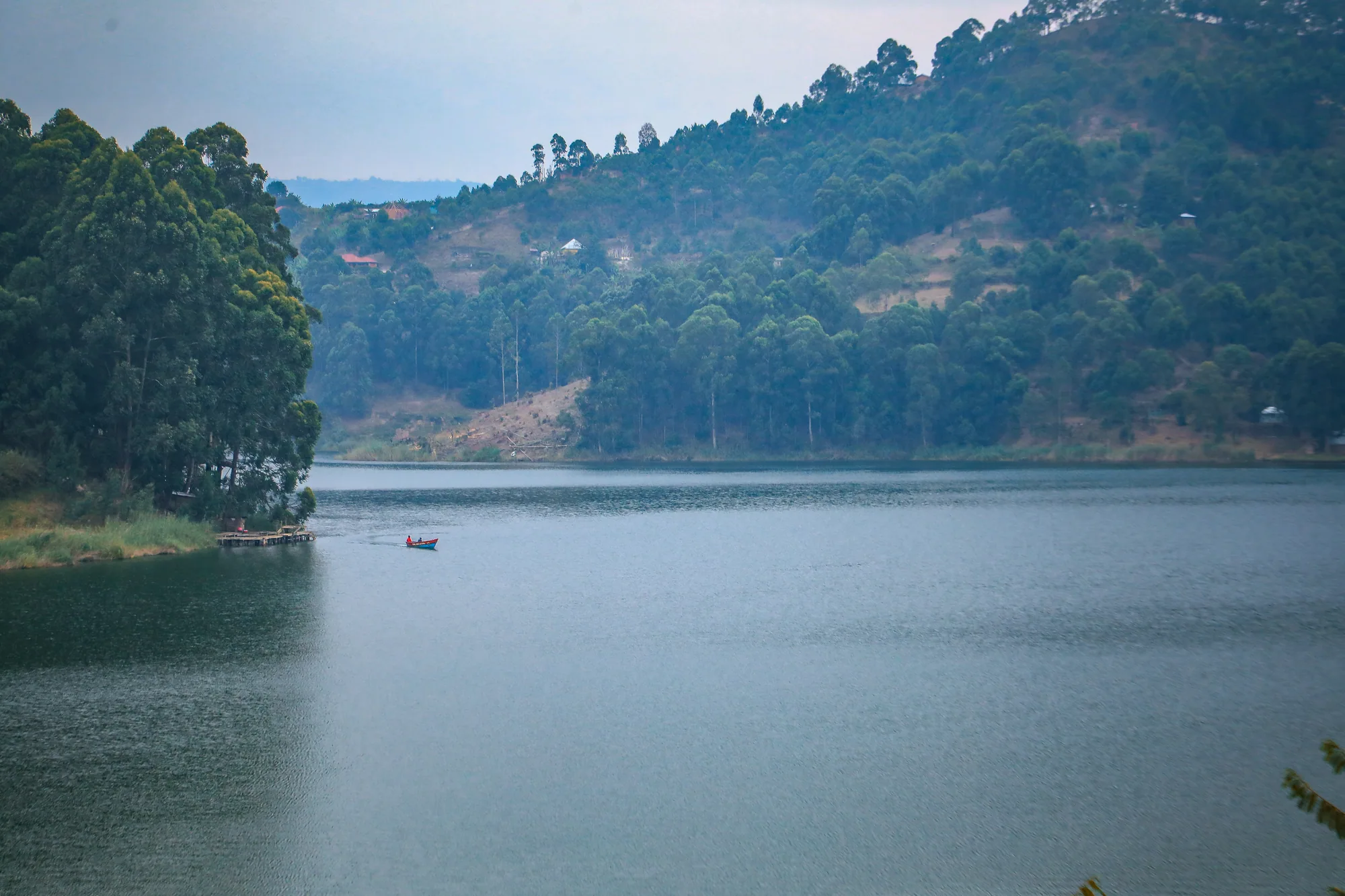 A wide reach of Lake Bunyonyi with a small boat and wooded ridges beyond