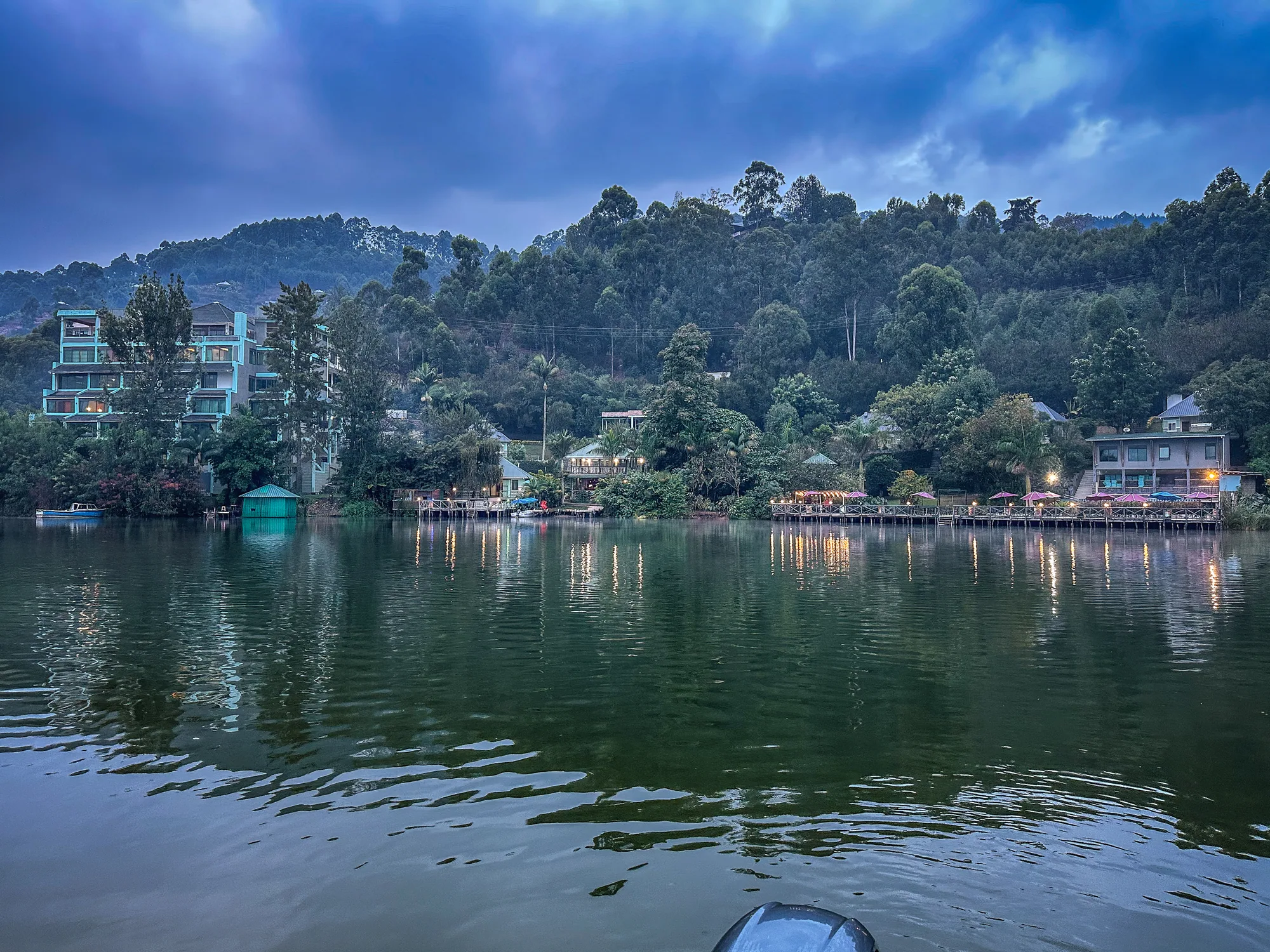 A broad bay of Lake Bunyonyi with the resort among trees on the far shore under a heavy sky